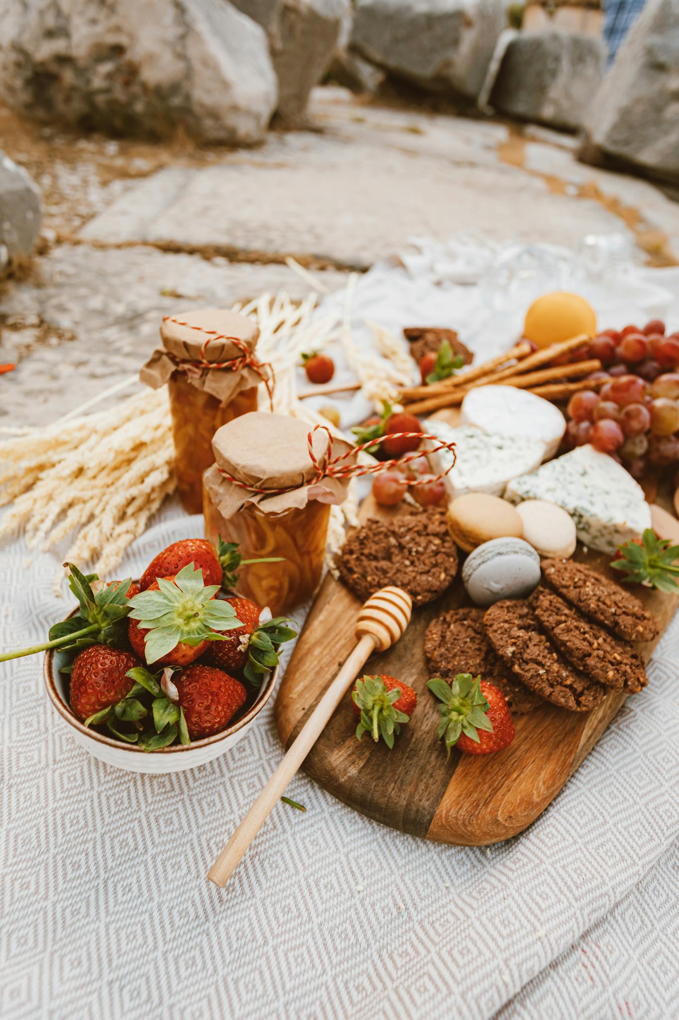 A rustic outdoor picnic with cheese, fruits, and homemade cookies on a wooden board.