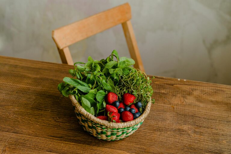 A woven basket filled with mint, strawberries, and blueberries on a wooden table.