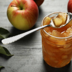 Tasty apple jam with spoon in glass jar and fresh fruits on grey table
