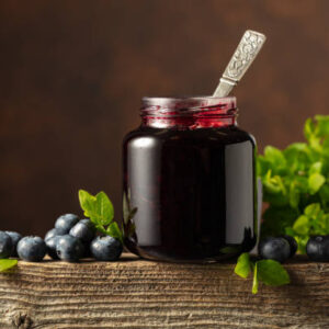 Jar of blueberry jam with fresh berries and leaves on an old wooden table.