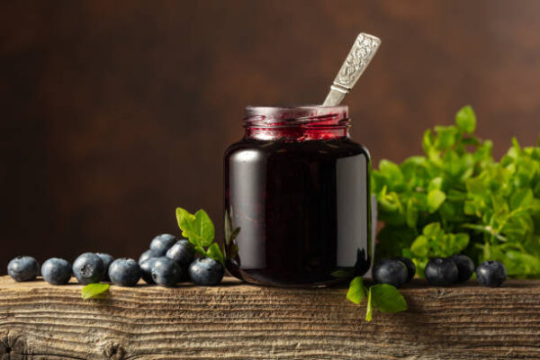 Jar of blueberry jam with fresh berries and leaves on an old wooden table.