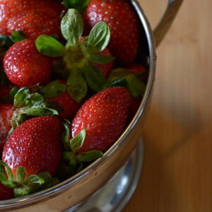 Close up image os strawberries in a colander on a wood cutting board