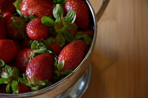 Close up image os strawberries in a colander on a wood cutting board