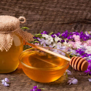 Jar of honey with wildflowers on old wooden background.