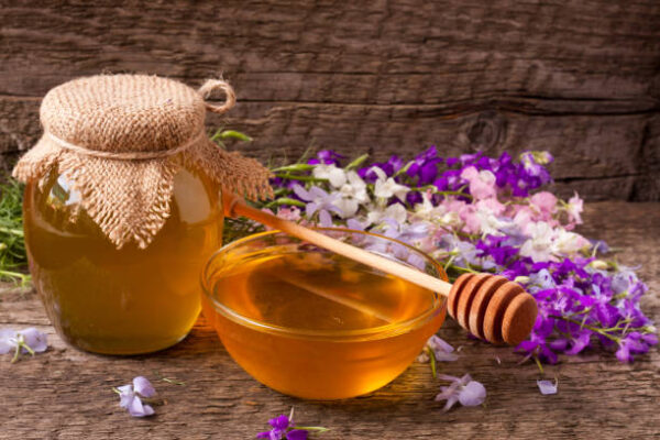 Jar of honey with wildflowers on old wooden background.