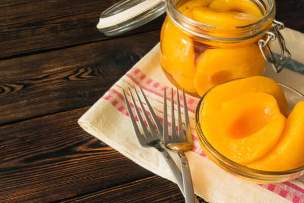 Peach canned in a glass jar and bowl on a dark wooden background