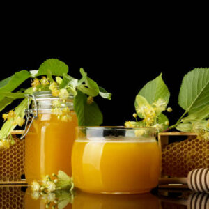 Two glass jars with honey and blossom of linden isolated on black background